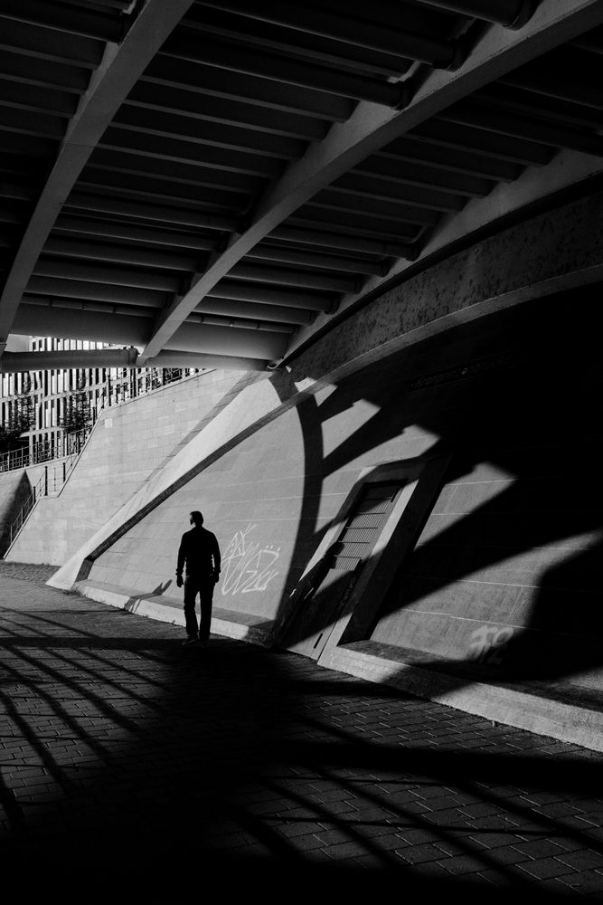 Grayscale photo of man walking on sidewalk in a tunnel