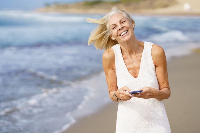Happy older female using her phone on a rocky beach
