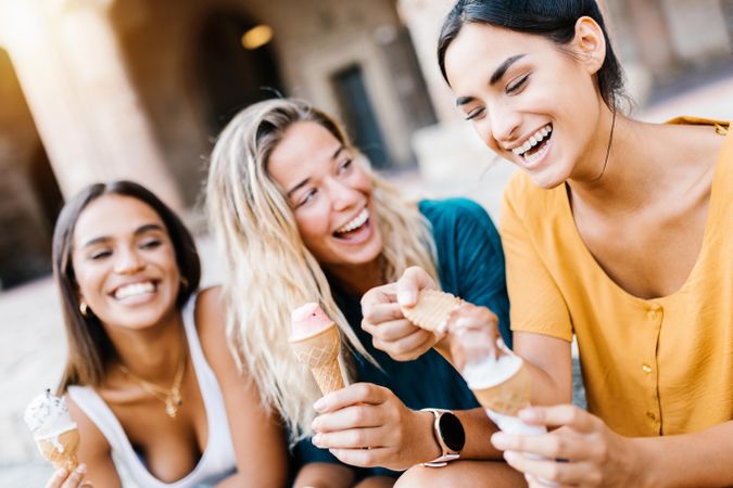 Happy multi-ethnic women laughing together outdoors while eating ice cream