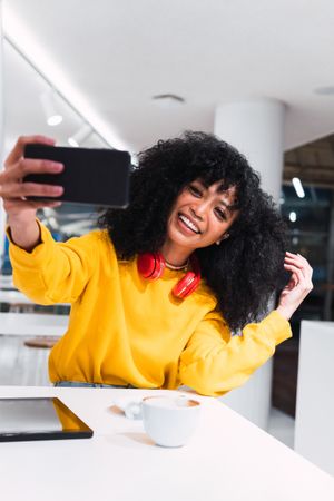 Excited young woman smiling and taking selfie in cafe