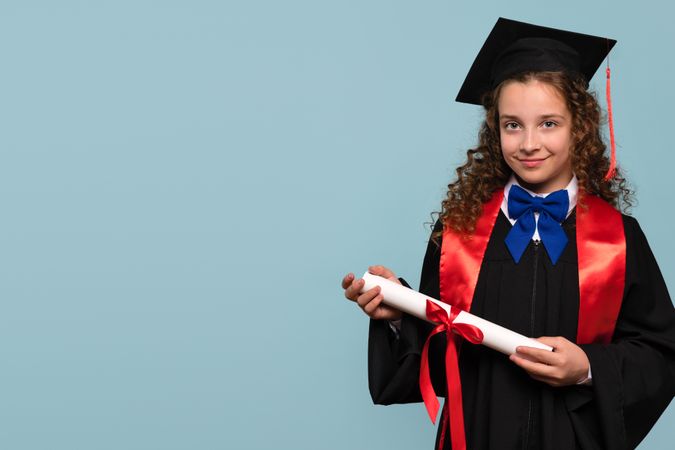 Young girl in graduation gown holding diploma, smiling confidently.