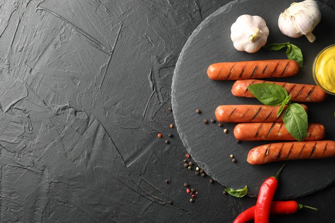 Grilled sausages or hot dogs on dark ceramic plate with garlic and mustard, copy space