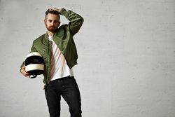 Man in green jacket holding biker helmet in studio shoot with hand on head