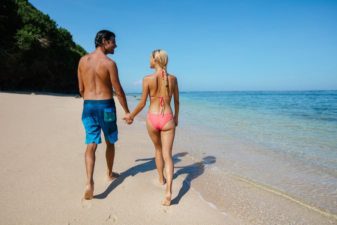 Honeymoon couple holding hands walking on beach