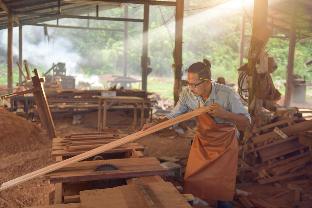 Carpenter cutting a piece of wood with the machine