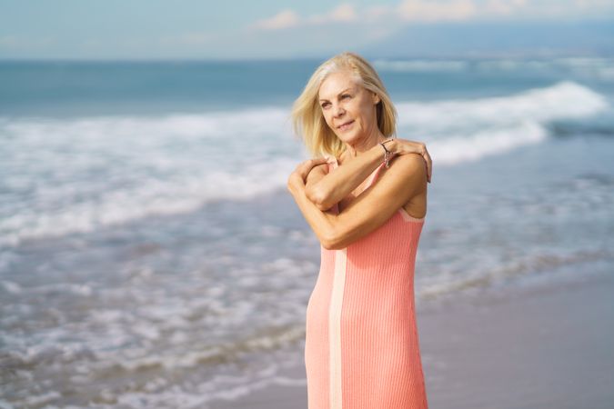 Serene older woman smiling while standing in the sand on a beach