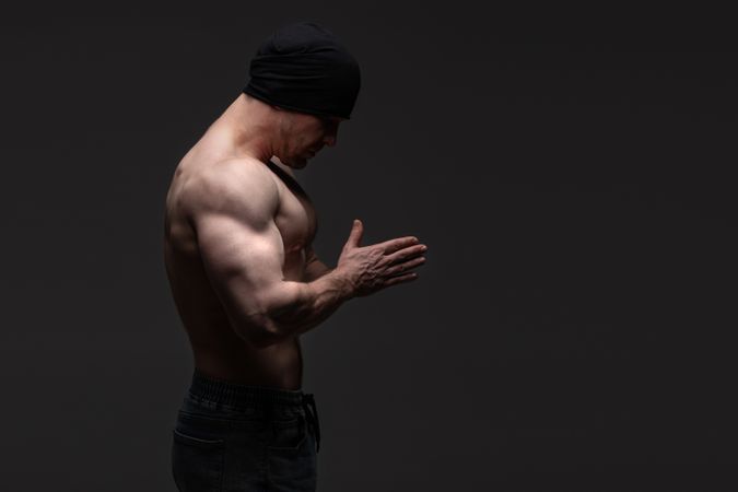 Shirtless man in beanie with hands together, contemplative posture