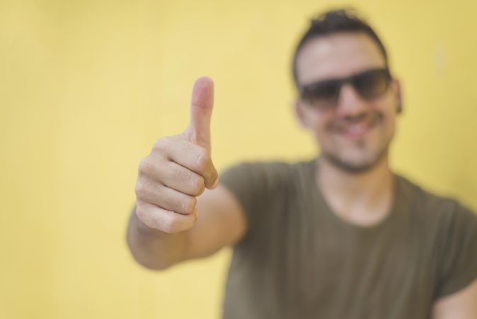 Smiling male with thumbs up in front of yellow wall outside