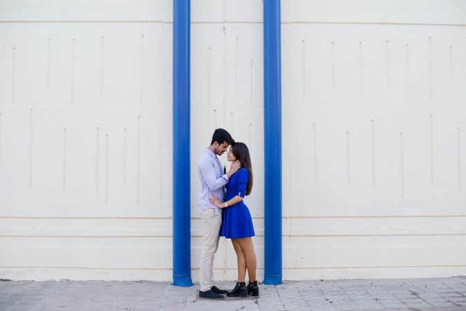 Amorous couple standing against white wall with blue columns