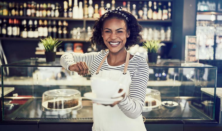 Smiling woman serving coffee in front of modern bar