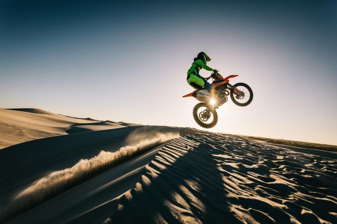 Dirt biker riding mid air over a sand dune in desert
