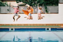 two young women and a man jumping by the pool