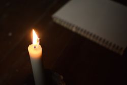 Top view of candle lit in the dark next to notebook