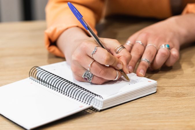 Crop woman taking notes in notebook during work in cafe