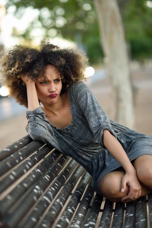 Befuddled female in casual dress sitting on park bench looking around, copy space