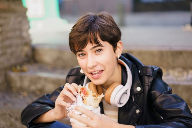A young person joyfully enjoys a delicious burrito while relaxing outdoors in the city