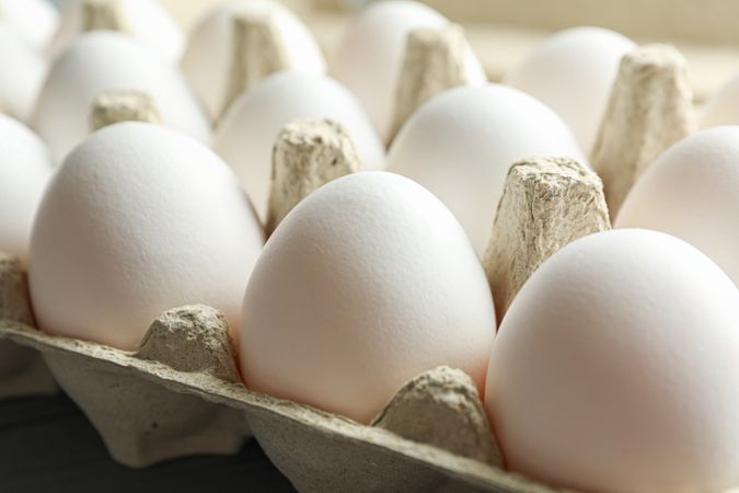 chicken eggs in carton box on wooden table, closeup