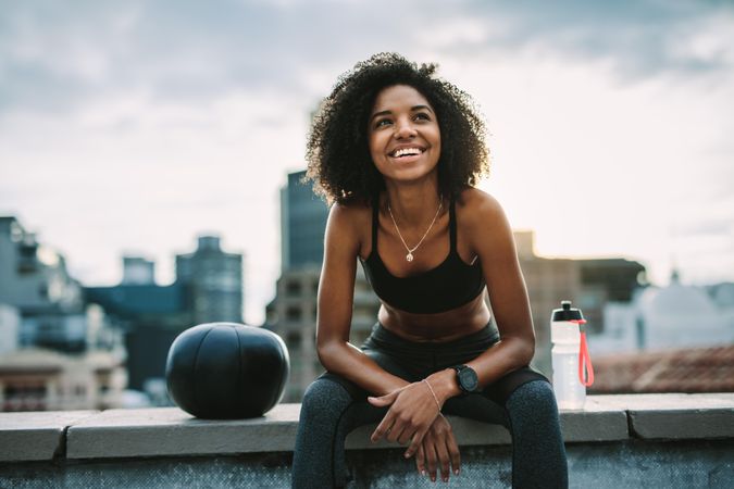 Fitness woman relaxing sitting on rooftop fence looking away
