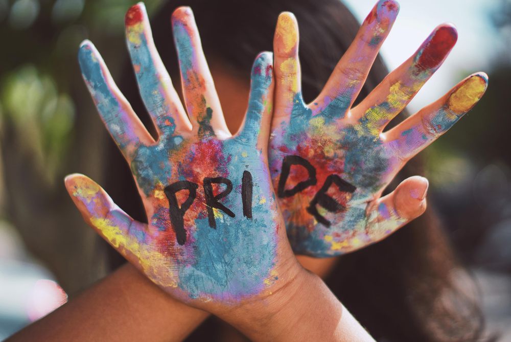 Painted hands with "Pride" written on them covering person's face 