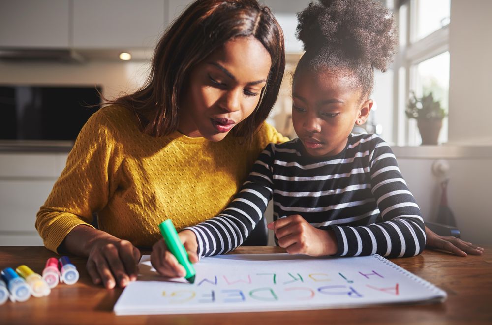 Daughter writing out alphabet as mother looks on
