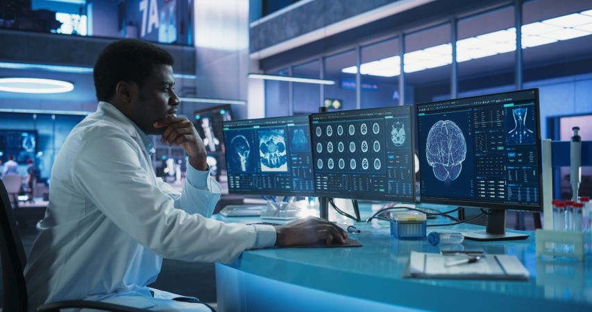 Cancer Research Center Medical Laboratory: Black Male Neuroscientist Using Desktop Computer To Analyze CT Scans Of Human Brain.