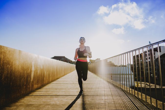 Woman running on walkway in sunny day with blue sky