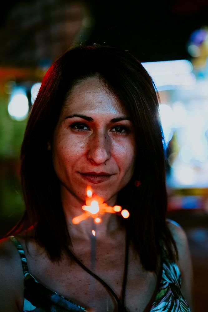 Woman holding sparkler on fairground in evening
