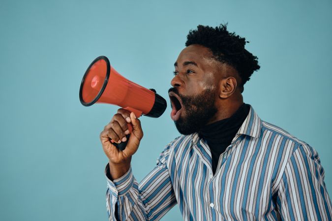 Portrait of a Black man in blue studio shoot yelling into megaphone