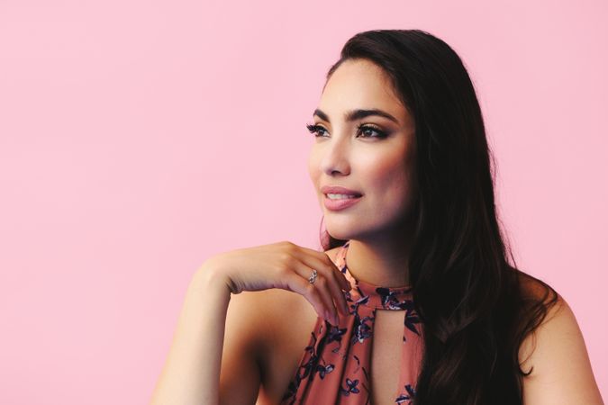 Serious Hispanic woman resting chin on her hand in pink room