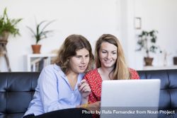 Two young women using computer while sitting on couch 432l8Z