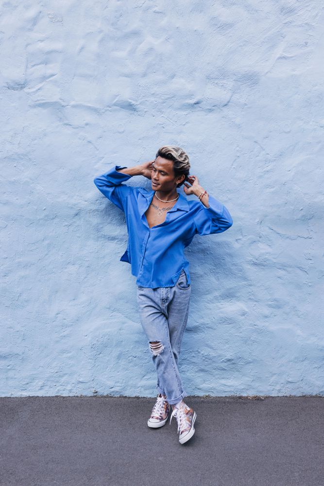 Man in a blue shirt leaning wall outdoors while running his hands through hair, vertical