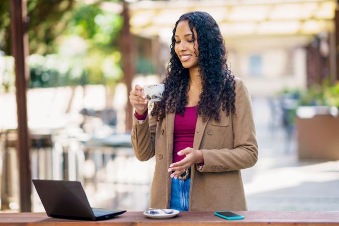 A Professional Woman is Enjoying a Cup of Coffee Outdoors While Using Her Laptop