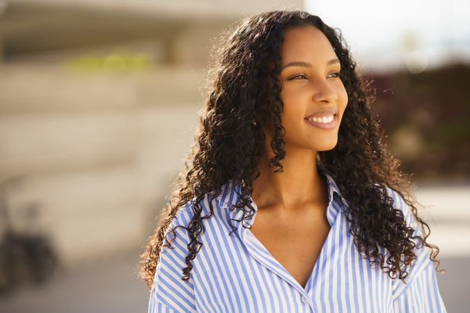 A smiling young woman with curly hair enjoying the outdoors, radiating joy and positivity