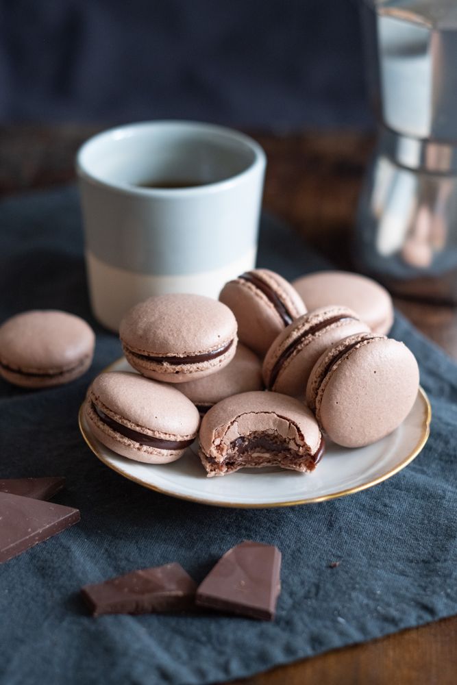 Tasty chocolate macarons, chocolate chunks, and coffee mug on table