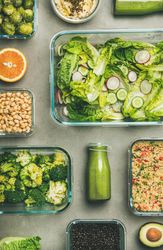 Variety of vegetable dishes in glass containers with bottles of dressing, vertical composition