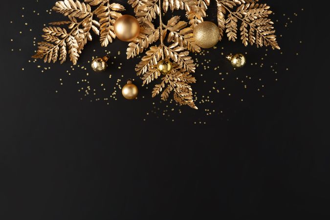 Golden holiday decorations, glitter, baubles and leaves on dark background