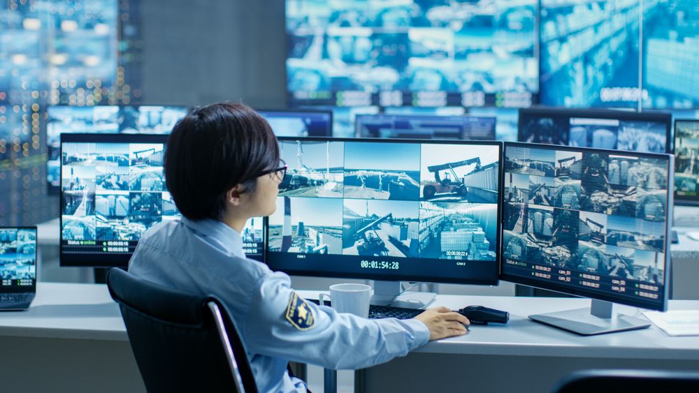 In the Security Control Room Officer Monitors Multiple Screens for Suspicious Activities, He Drinks from a Mug.