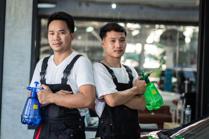 Two men in overalls standing in auto detail shop holding water bottles