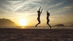 Silhouettes of two little girls jumping in the beach at sunset