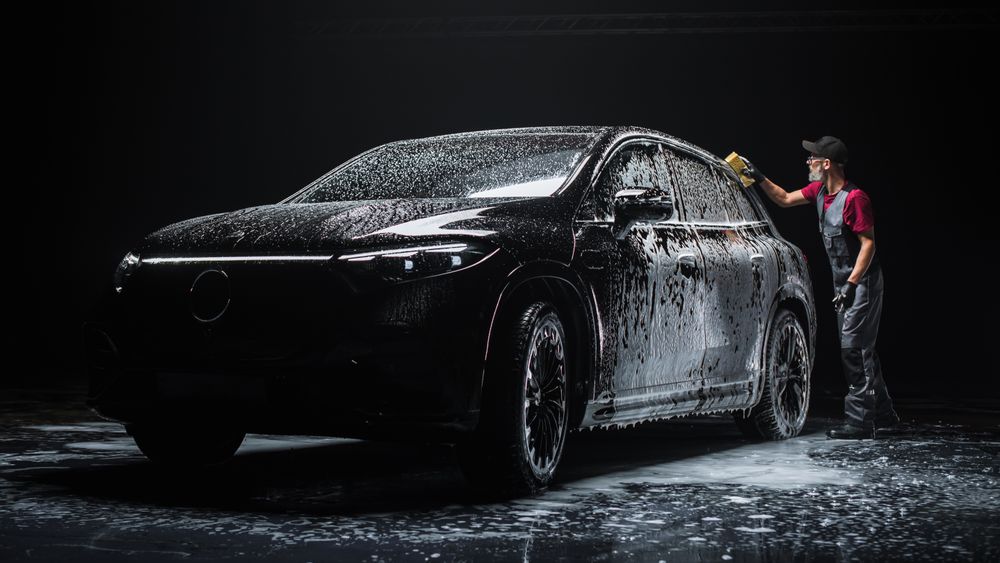 Professional Car Wash Specialist Spreading Foam with a Soft Sponge to Prepare a Modern Electric SUV with Contemporary Design at a Dealership Car Center.