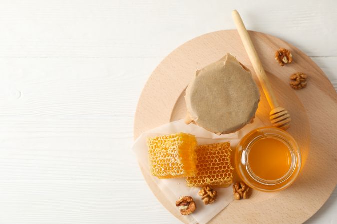 Honeycombs, walnuts, dipper and jars with honey on wooden background, top view