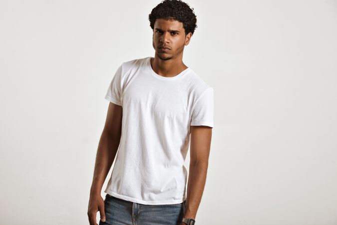 Man in blank t-shirt and jeans leaning slightly with serious expression in studio shoot