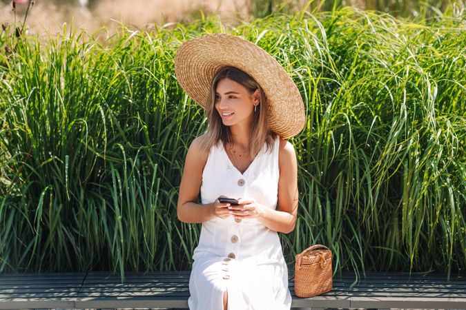 Woman sitting in front of long grass looking away while holding cell phone
