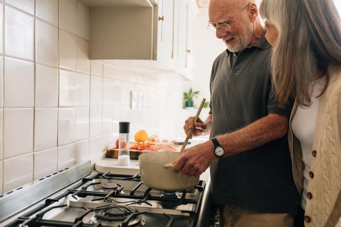 Older man cooking food while his wife is talking to him