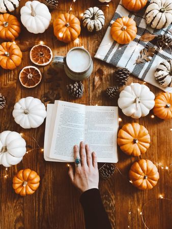 Woman holding book page between orange slices and pumpkins