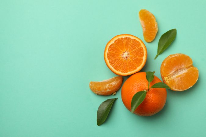 Ripe mandarins with leaves on mint background, top view