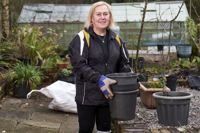 Older woman lifting empty pots in garden