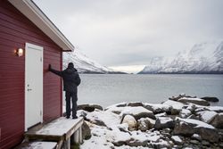 Solitary man on rocky shore against tranquil lake and snowy mountains in cold day