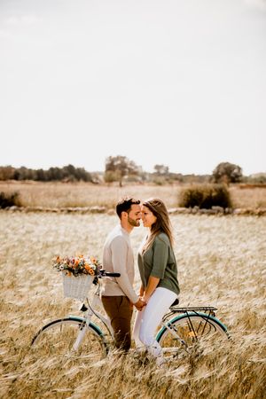 Sincere lovers posing by bicycle on rye field