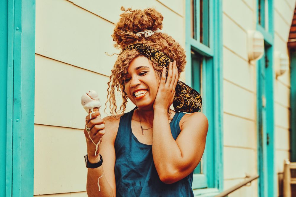 Entertained Black female snacking on an ice cream cone in the sun